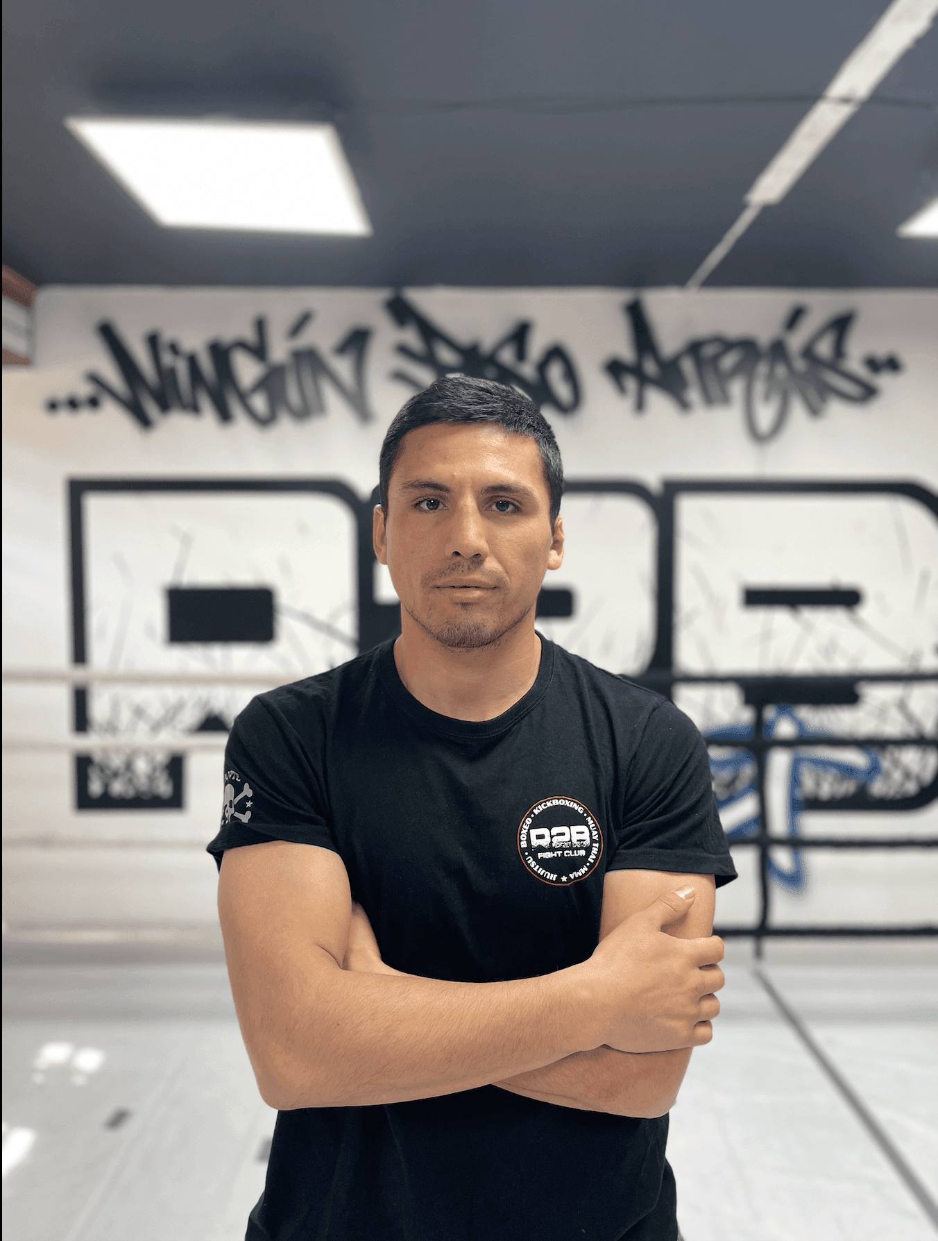 Man in a black shirt with arms crossed standing in front of a wall with graffiti art.