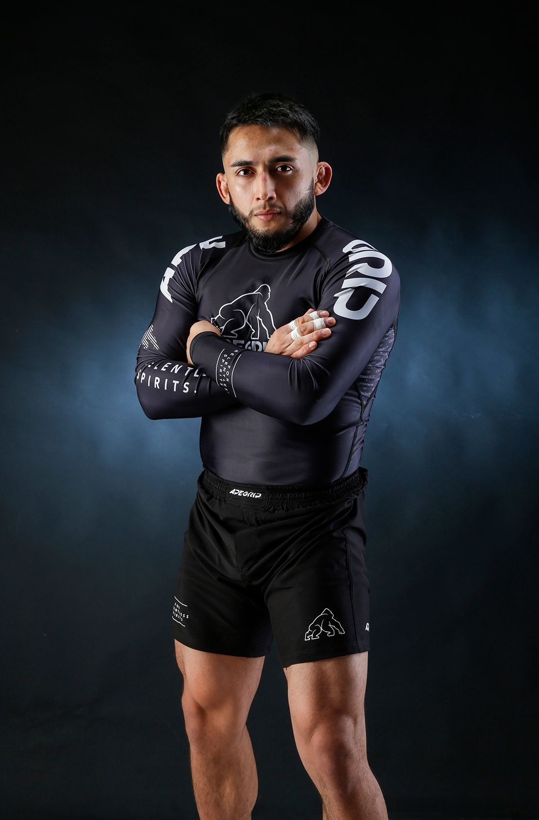 Man wearing black compression sportswear standing with arms crossed against a dark background.